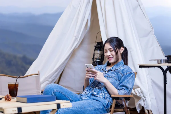 Asian woman reading book while on a solo trekking camp on the top of the mountain with small tent for weekend activities and outdoor pursuit
