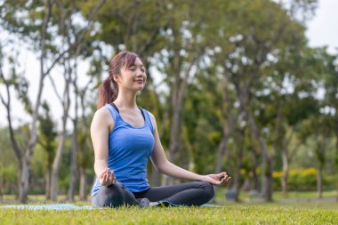 Yoga kıyafetli genç Asyalı kadın iç huzurundan mutluluk elde etmek için ormanda rahatça meditasyon yapıyor. Nefes alma egzersizi, sağlıklı akıl ve ruh sağlığıyla ilgili bilgelik.
