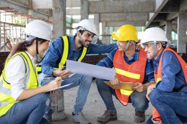 Mühendis, mimar, müteahhit ve ustabaşı ekibi inşaat sahasında gayrimenkul geliştirme projesi endüstrisi ve konut zaman çizelgesi için kat planıyla toplantı ve danışmanlık yapıyor.