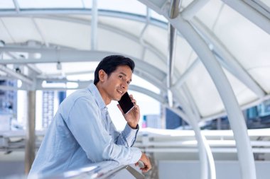 Asian man using mobile phone while walking along the urban metropolitan walk way in city downtown