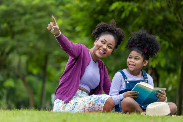 アフリカ系アメリカ人の教師は 教育と幸福のための公園で夏の屋外クラスを持っている間に読むために彼女の若い学生を教えています — ストック写真