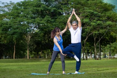 Kıdemli Asyalı adam bir bacağında denge yogası yapıyor. Kızı da halk parkında yaşlılar için uzun yaşam egzersizleri ve açık hava egzersizleri yapıyor.