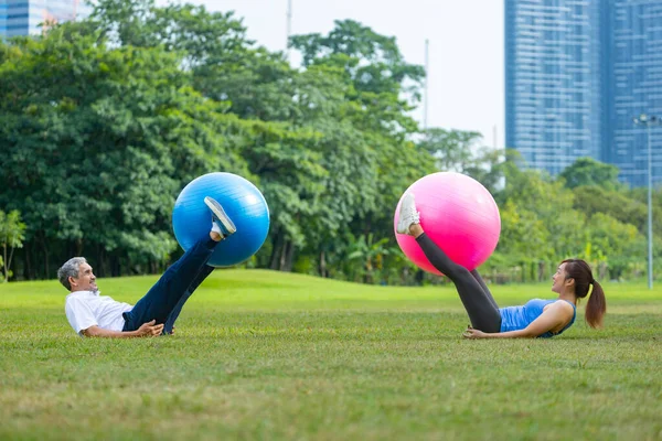 Senior asian man and his daughter are exercising with yoga ball in the public park to build core body muscle for elder longevity exercise and outdoor workout
