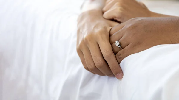 Close up hand of husband and wife holding together on the bed with wedding diamond ring on her finger for love, sensual, romance and intimacy relation