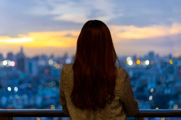 stock image Woman looking and enjoying sunset view from balcony with sun setting behind skyscraper in busy urban downtown with loneliness for solitude, loneliness and dreaming of freedom lifestyle