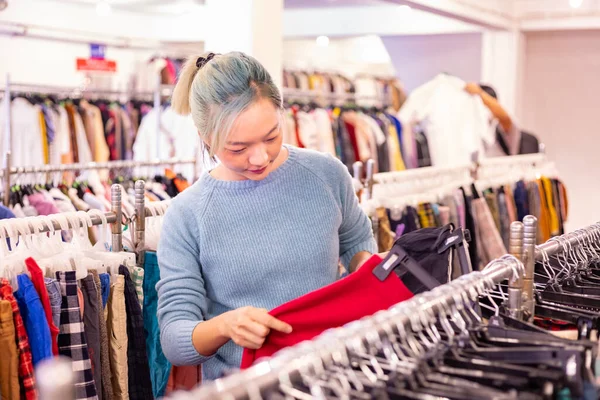 スタイリッシュなアジアの女性は 新しい年とクリスマスの休日に暖かく保つために冬のファッションのための衣料品店から中古のセーターを選択しています — ストック写真