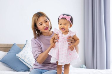 Asyalı anne güzel gülümseyen kızını kucağında tutarken aile mutluluğu ve ebeveynlik kavramı için yatakta kaliteli zaman geçiriyor.