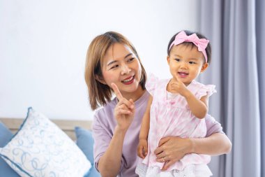 Asyalı anne güzel gülümseyen kızını kucağında tutarken aile mutluluğu ve ebeveynlik kavramı için yatakta kaliteli zaman geçiriyor.