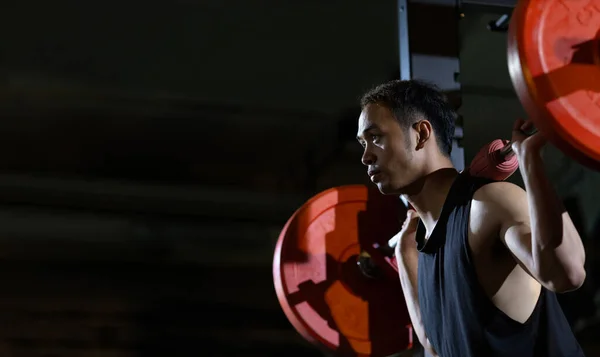 亚洲肌肉运动健美男子是在体操馆的核心肌肉的死力杠铃上进行举重训练的人 该运动健美的背景是黑暗的 — 图库照片