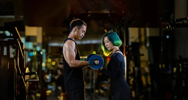 亚洲妇女在体操馆的臂膀肌肉的杠铃训练中 使用简易杠铃作为初学者 并得到教练的支持 以防止运动和锻炼时受伤 黑暗的背景 — 图库照片