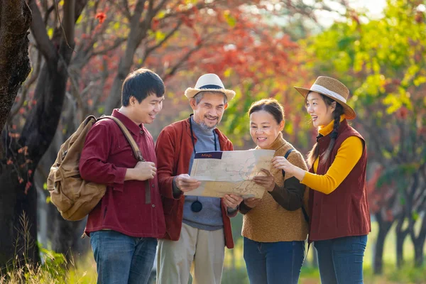 Happy Asian family with senior parent walking together in public park during autumn with maple and ginkgo tree while looking at map for fall color travel destination and family happy vacation