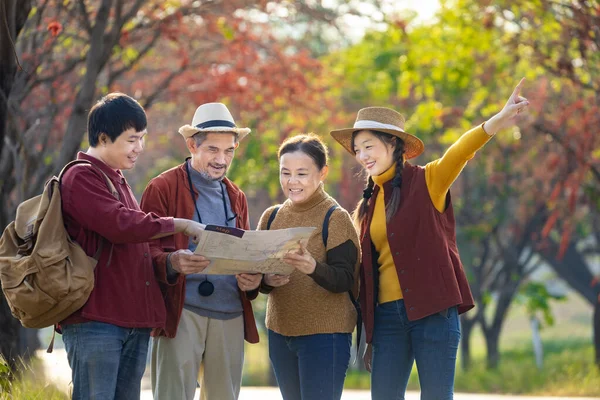 Happy Asian family with senior parent walking together at public park during autumn with maple and ginkgo tree while looking at map for fall color travel destination and family happy vacation