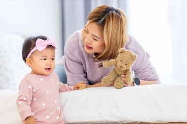 Asyalı anne güzel gülümseyen kızını kucağında tutarken aile mutluluğu ve ebeveynlik kullanımı için yatakta kaliteli zaman geçiriyor.