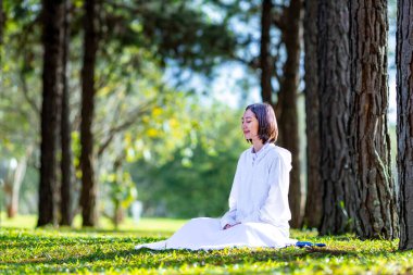 Kadın rahat bir şekilde çam ormanında meditasyon yapıyor. Sağlıklı zihin ve ruh kullanımı için sabah ışığı ile iç huzur bilgeliğinden mutluluk elde etmek için.