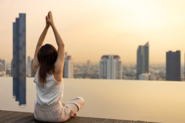Yüzme havuzunun çatısında rahatça yoga meditasyonu yapan bir kadın. İç huzur bilgeliğinden mutluluk elde etmek için gökyüzü manzaralı bir yer.