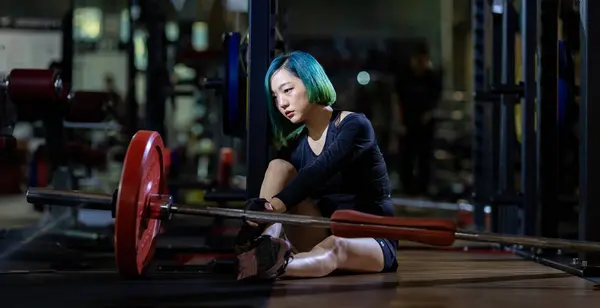 亚洲女人在健身房进行体重训练后 正面临着体重增加综合症 体能训练和健身的背景都很暗 — 图库照片