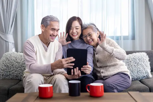 Asian family reunion of senior father mother and daughter sitting on couch with happy smile in retirement home while having video call to others relation and cousin member