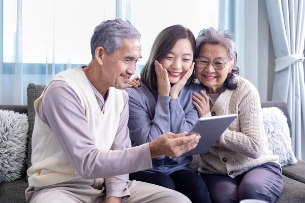 Asian family reunion of senior father, mother and daughter sitting on couch with happy smile in retirement home while looking at old nostalgic photo in the past