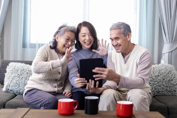 Asian family reunion of senior father mother and daughter sitting on couch with happy smile in retirement home while having video call to other relations and cousin member