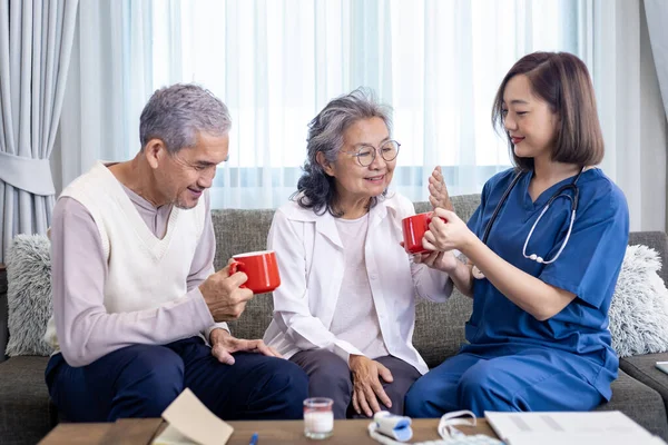 Senior couple get medical advice visit from caregiver nutritionist at home while having suggestion on herbal hot chamomile tea drink for longevity, healthy sleep and cure to insomnia concept