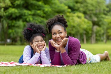 Afrika kökenli Amerikalı anne ve küçük kızı hafta sonu eğlence ve mutluluk için halka açık parkta piknik yaptıktan sonra uzanıyorlar.