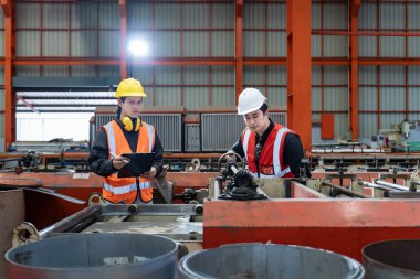 Asyalı endüstriyel işçiler, güvenlik sanayii için çatı fabrikasında çalışırken otomatik monitörle metal levha oluşturma makinesinin kurulum değerini kontrol ediyorlar.