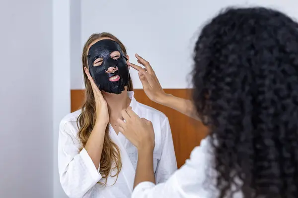 Couple of girlfriend in bathrobe doing skincare routine using facial mask on the spa holiday for beauty skin and treatment