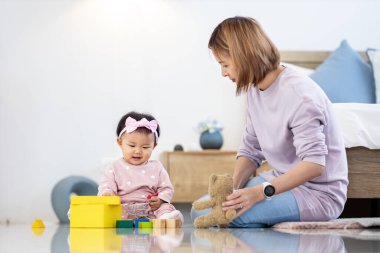 Asyalı anne, güzel gülümseyen kızıyla tahta oyuncak bloğuyla oynarken aile mutluluğu ve ebeveynlik için yatakta kaliteli zaman geçiriyor.