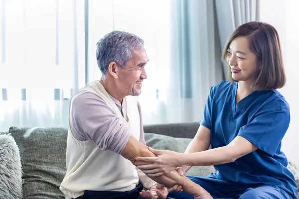 Senior Asian man got medical service visit from caregiver nurse at home while preparing for physical therapy and using ointment rubbing for muscle pain in health care and pension welfare