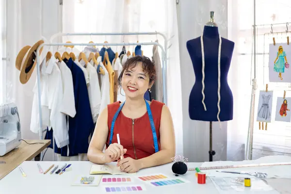 ファッショナブルなフリーランスのドレスメーカーは ファッションデザインと衣料品ビジネス業界のための芸術的なワークショップスタジオで働いている間 イラストレーターを描くことによって新しいドレスを設計しています — ストック写真
