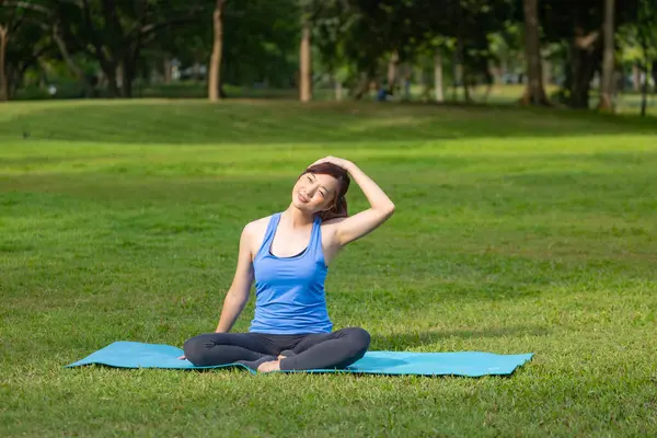 Asyalı kadın halka açık parkta egzersiz yaptıktan sonra serinlemek için yoga yapıyor.