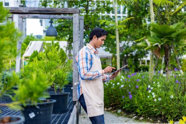 Asyalı bahçıvan, yerli ve egzotik bitki yetiştiricileri için çocuk bahçesi merkezinde çalışırken dijital tablet kullanıyor.