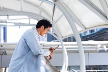 Asyalı adam şehir merkezindeki Bangkok yolunda yürürken cep telefonu kullanıyor.