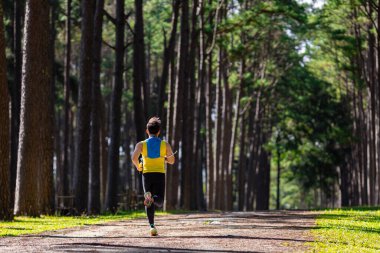 Asyalı patika koşucusu çam ormanlarının toprak yolunda koşuyor. Sırt çantasıyla birlikte sağlıklı yaşam tarzı ve formda kalmak için ultra maratonda egzersiz eğitimi alıyor.