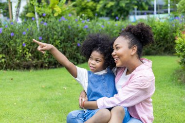 Afrika kökenli Amerikalı anne, refah ve mutluluk için halka açık parkta yaz pikniği yaparken genç kızıyla ata binme oyunu oynuyor.