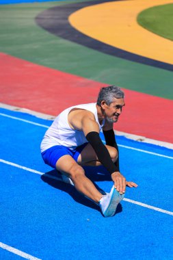 Kıdemli Asyalı atlet profesyonel egzersiz, spor antrenmanı ve uzun yaşam için sağlıklı olan profesyonel mavi pistte koşmak için ısınma hareketleri yapıyor.