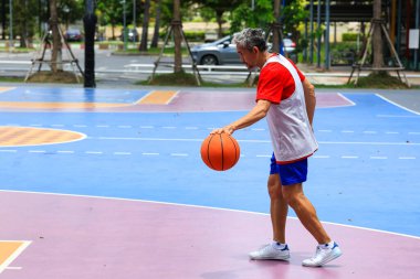 Yaşlılığa karşı egzersiz yapmak ve egzersiz yapmak için sağlıklı ve eğlenceli aktiviteler için dışarıda basketbol oynayan emekli Asyalı kıdemli bir adam.