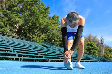 Kıdemli Asyalı atlet profesyonel egzersiz, spor antrenmanı ve uzun yaşam için sağlıklı olan profesyonel mavi pistte koşmak için ısınma hareketleri yapıyor.
