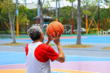Yaşlılığa karşı egzersiz yapmak ve egzersiz yapmak için sağlıklı ve eğlenceli aktiviteler için dışarıda basketbol oynayan emekli Asyalı kıdemli bir adam.