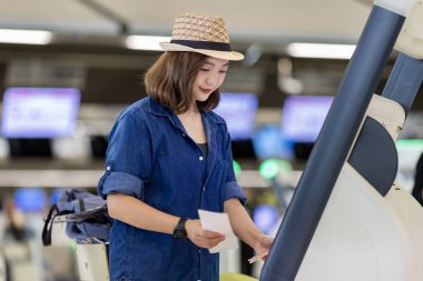 Bagajı taşıyan genç Asyalı kadın yolcu uluslararası seyahat ve tatil uçuşu için havaalanı terminalinde kendi kendini kontrol ediyor. 