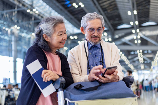 Senior Asian couple tourist  passenger is looking at the boarding pass from online self check in in at airport terminal for international travel flight and vacation