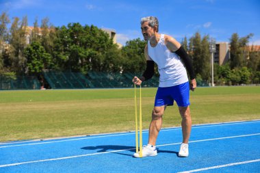 Kıdemli Asyalı atlet profesyonel egzersiz, spor antrenmanı ve uzun yaşam konsepti için sağlıklı olan profesyonel mavi pistte koşmak için lastik bant kullanıyor.