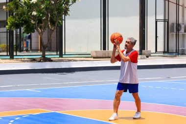 Yaşlılığa karşı egzersiz yapmak ve egzersiz yapmak için sağlıklı ve eğlenceli aktiviteler için dışarıda basketbol oynayan emekli Asyalı kıdemli bir adam.