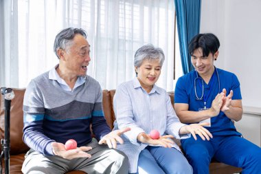 Yaşlı çift, erkek bakıcı hemşirelerden sağlık hizmeti alırken emeklilik merkezinde kas gücü ve iyileşme süreci için yumuşak top kullanılıyor.