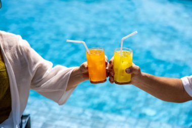 Kıdemli Asyalı çift yaz tatili için tropikal tatil otelinde yüzme havuzunun yanında meyve suyu içti ve sağlıklı yaşlanma aktiviteleri için yaşlı ve mutlu emekliler.