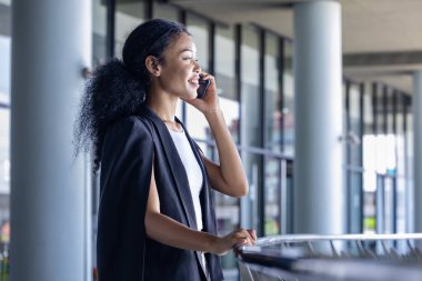 Lüks Afrikalı genç CEO kadın girişimci iş iletişimi ve kentsel yaşam tarzı kavramı için arka planda modern ofis ile cep telefonu kullanıyor.