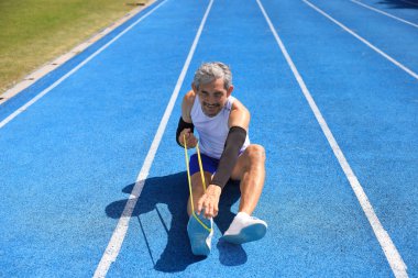Kıdemli Asyalı atlet profesyonel egzersiz, spor antrenmanı ve uzun yaşam konsepti için sağlıklı olan profesyonel mavi pistte koşmak için lastik bant kullanıyor.
