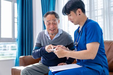 Kıdemli yaşlı adam, sağlık ve emeklilik sigortası için termometre sağlık muayenesi ve emeklilik sigortası nedeniyle vücut ısısı nedeniyle evde erkek bakıcı tarafından ziyaret ediliyor.