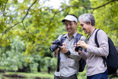 Asyalı son sınıf öğrencisi ve oğlu hafta sonu tatili macerası ve aile aktiviteleri konsepti için yaban hayatının fotoğraflarını çekerken ormanda geziniyorlar.