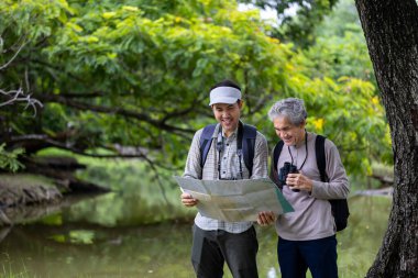 Asya 'lı son sınıf öğrencisi ve oğlu hafta sonu tatili macerası ve aile aktiviteleri için haritaya bakarken ormanda geziniyorlar.